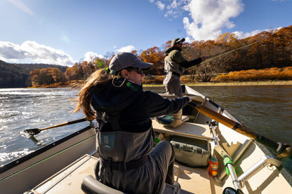 A person rowing a drift boat on a river surrounded by autumn-colored trees.
